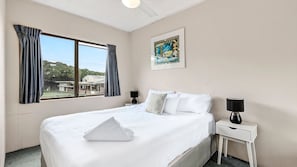 Ein Hotelzimmer mit einem großen Bett, einem Fenster mit Vorhängen, einem Nachttisch mit Lampe und einem gerahmten Bild an der Wand.