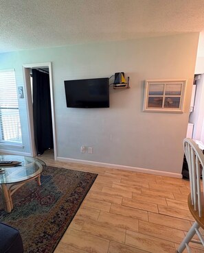 Un salon avec un téléviseur à écran plat fixé au mur, un tapis à motifs et un plancher en bois.
