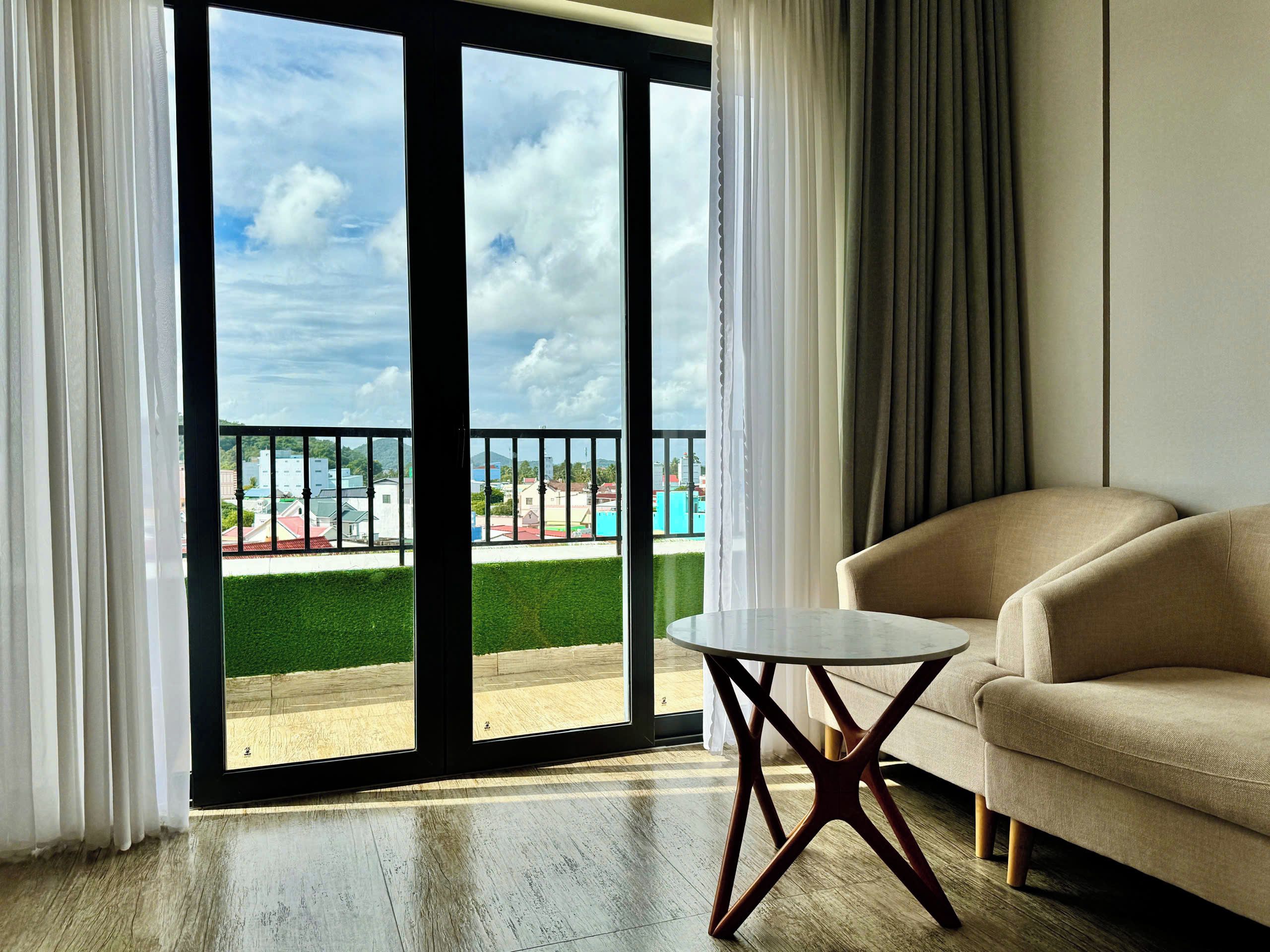 A room with a sofa, a small table, and a view of a green lawn and buildings through a glass door.