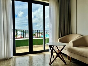 Una habitación con un sofá, una mesita y vistas a un césped verde y edificios a través de un ventanal.
