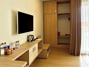 A hotel room with a flat-screen TV, wooden furniture, a coffee maker, and a wardrobe.