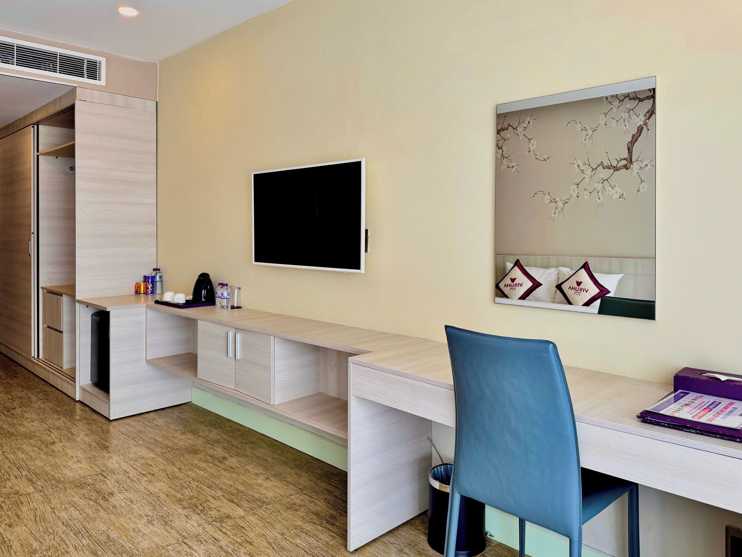 A hotel room with a desk, chair, TV, and a large mirror.