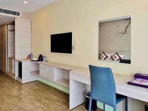 Habitación de hotel con escritorio, silla, televisión y un espejo grande.
