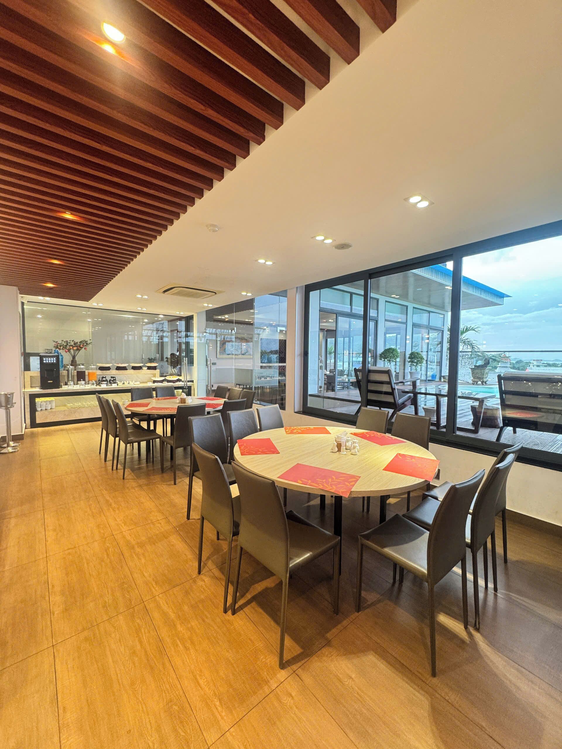 A modern dining area with round tables, chairs, and large windows offering a view of the outdoors.