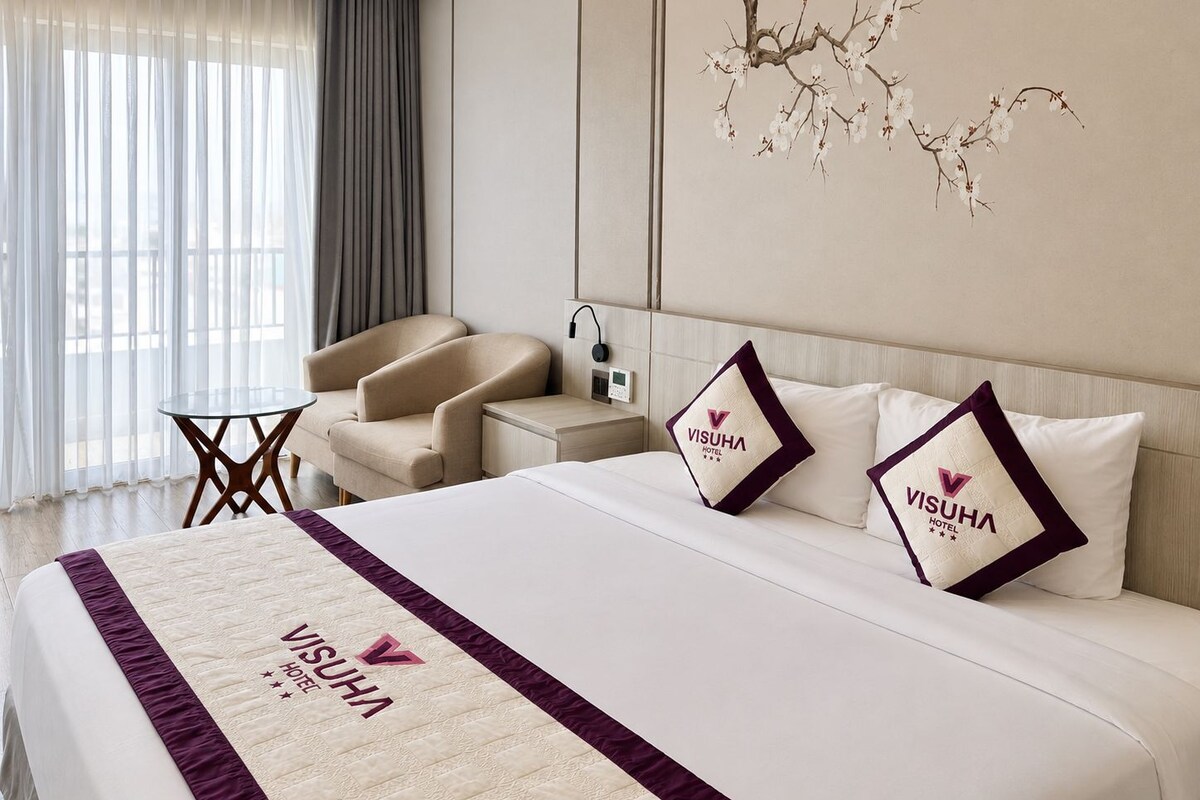 A hotel room with a bed, a chair, a small table, and a wall-mounted artwork.