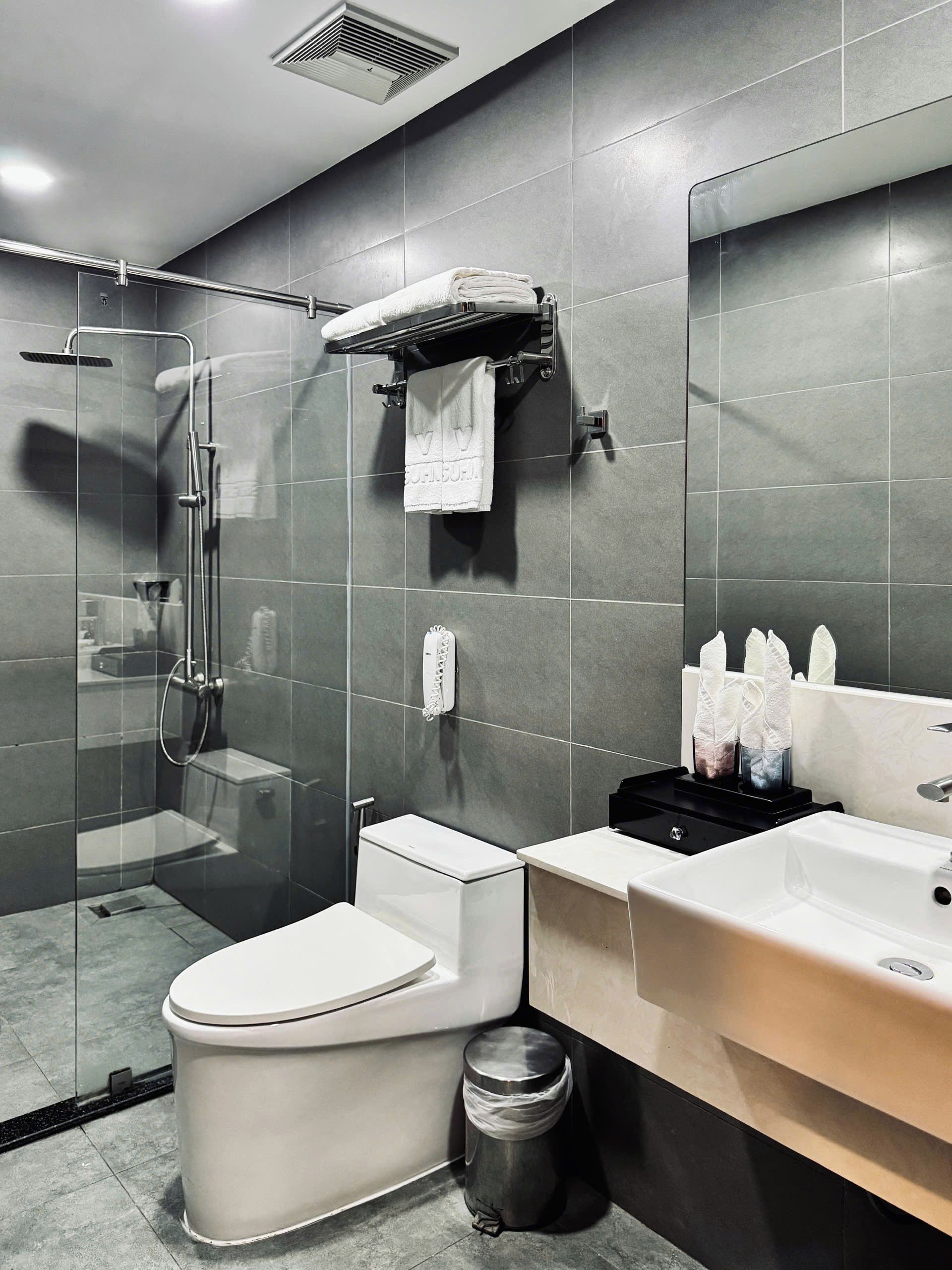 Un baño moderno con ducha de vidrio, inodoro, lavamanos y un cubo de basura.