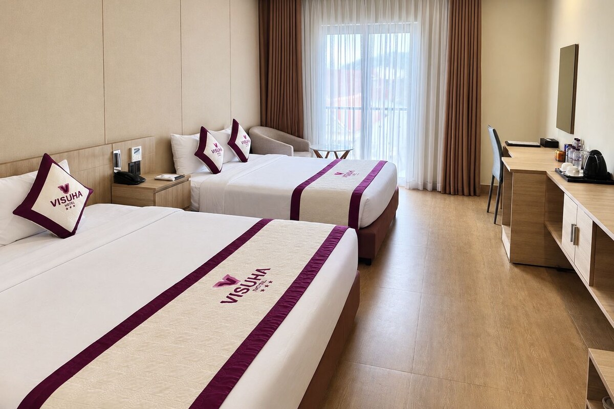 A hotel room with two beds, a desk, a chair, a TV, and a window with curtains.