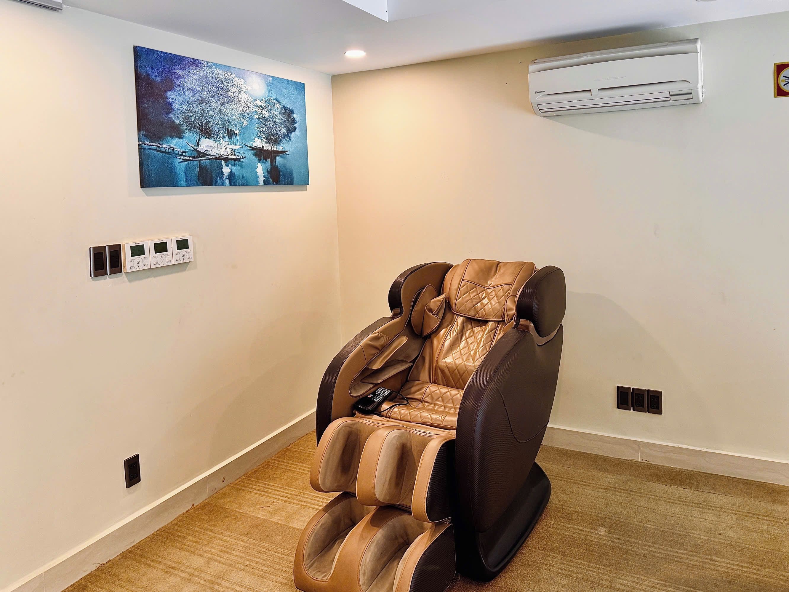 Una silla de masaje en una habitación con un cuadro en la pared y un equipo de aire acondicionado.