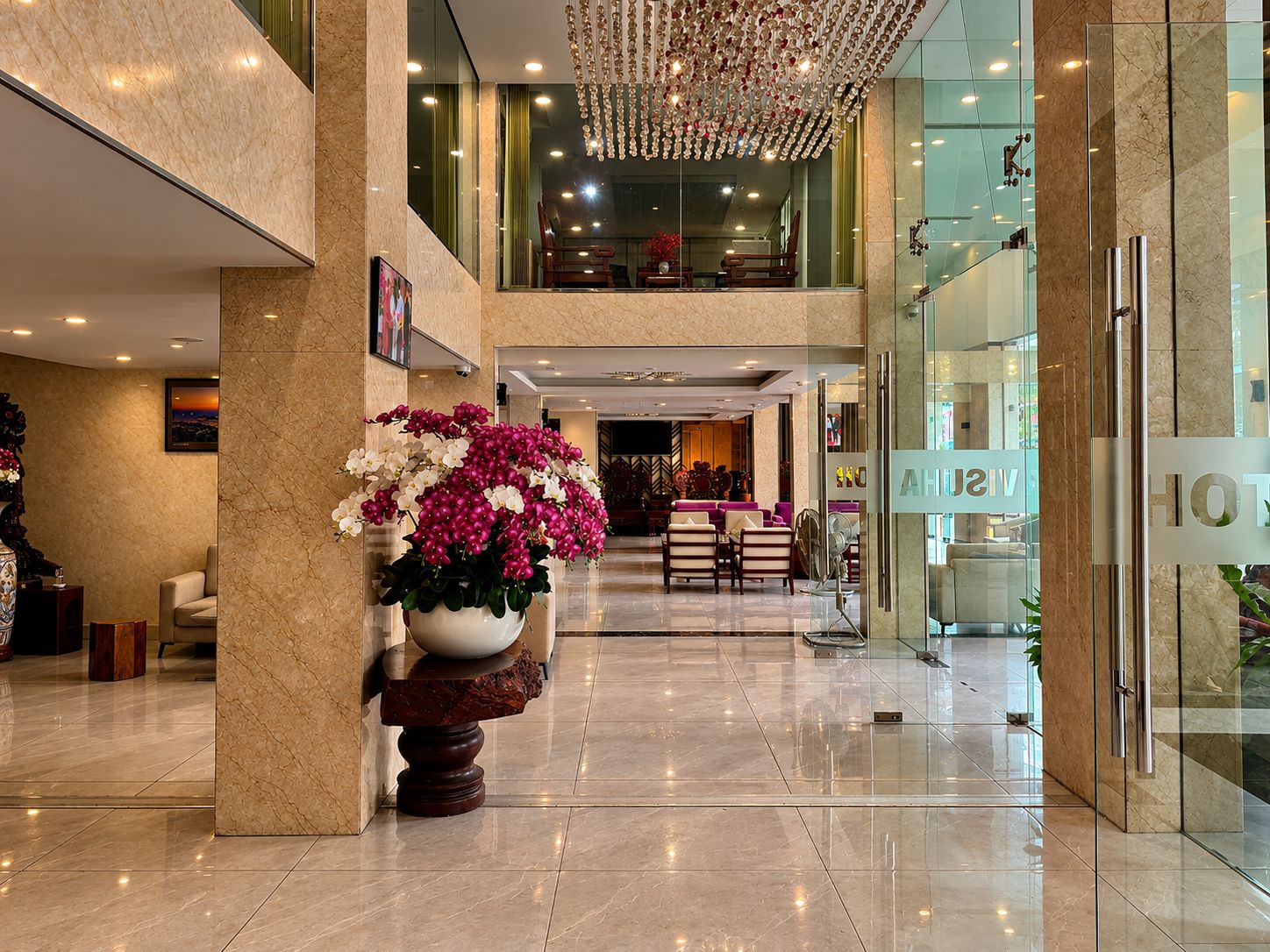 Um saguão de hotel com um arranjo floral grande, área de estar e vista do interior.