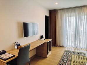 A modern hotel room with a flat-screen TV mounted on the wall, a wooden desk with a chair, a coffee maker, and a patterned rug on the floor.