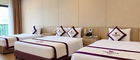 A hotel room with three beds, each with a matching headboard and pillow, and a bedside table with a phone and a lamp.