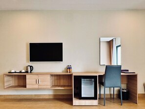 A compact hotel room with a wooden desk, a small refrigerator, a chair, a flat-screen TV, and a mirror. - VISUHA HOTEL   (Ha Tien)