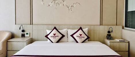 A hotel room with a bed, two pillows with the hotel logo, a nightstand with a phone, and a wall art piece.