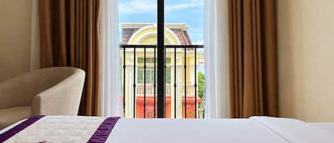 A hotel room with a bed, a chair, and a view of a building through a window with curtains.