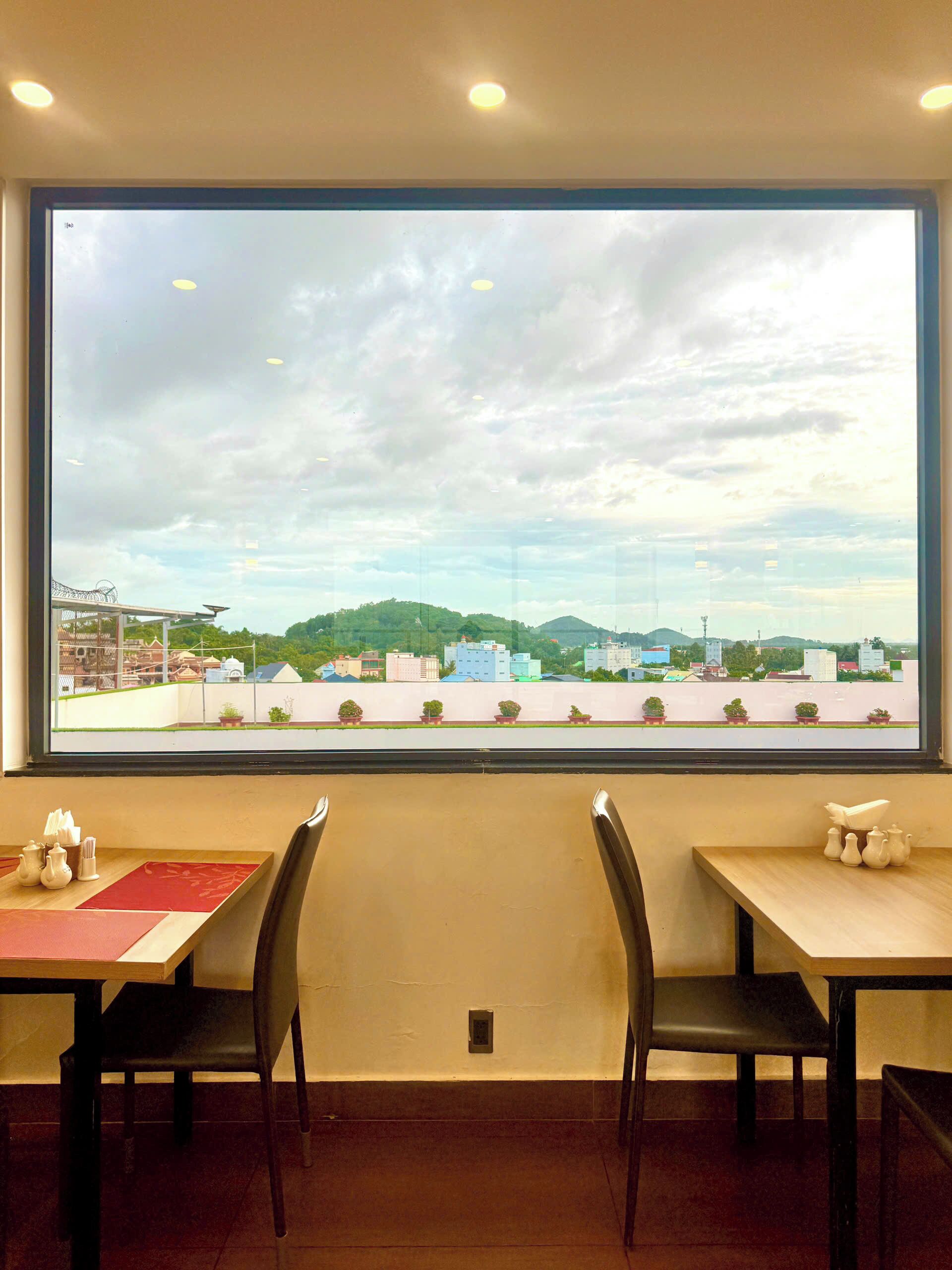 A dining area with a large window view of a cityscape, including buildings and greenery.