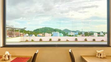 A dining area with a large window view of a cityscape, including buildings and greenery.