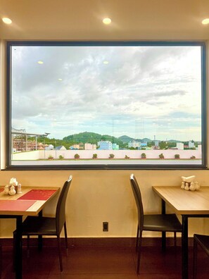 A dining area with a large window view of a cityscape, including buildings and greenery.