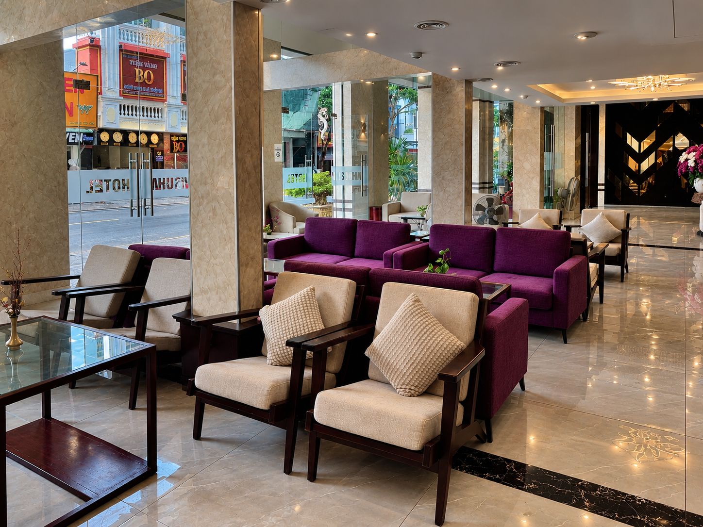 En hotelllobby med sittgrupper, ett soffbord i glas och utsikt över gatan utanför.