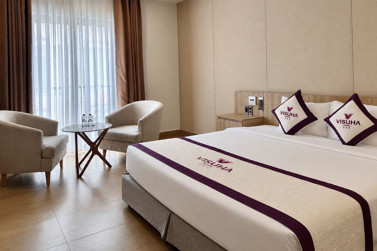 A hotel room with a bed, two armchairs, a small table, and a nightstand with a lamp.