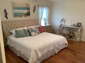 A bedroom with a large bed, a nightstand, a dresser, a wall-mounted bird sculpture, and a painting of the ocean. - Spacious 3br/2bth Wildwood Condo — Walk to the Beach, Boardwalk & Downtown! (Wildwood)