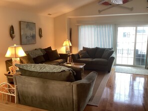 A living room with two couches, a coffee table, and two lamps. There is a window with blinds and a view of buildings outside. - Spacious 3br/2bth Wildwood Condo — Walk to the Beach, Boardwalk & Downtown! (Wildwood)