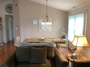A living room with a sofa, a dining table with chairs, a chandelier, and a lamp. - Spacious 3br/2bth Wildwood Condo — Walk to the Beach, Boardwalk & Downtown! (Wildwood)