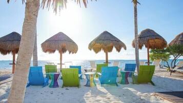 Una playa con sombrillas de paja y sillas de descanso coloridas.