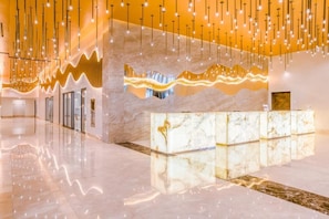 En modern hotellobby med en receptionsdisk i marmor, hängande lampor och en vågformad väggdesign.