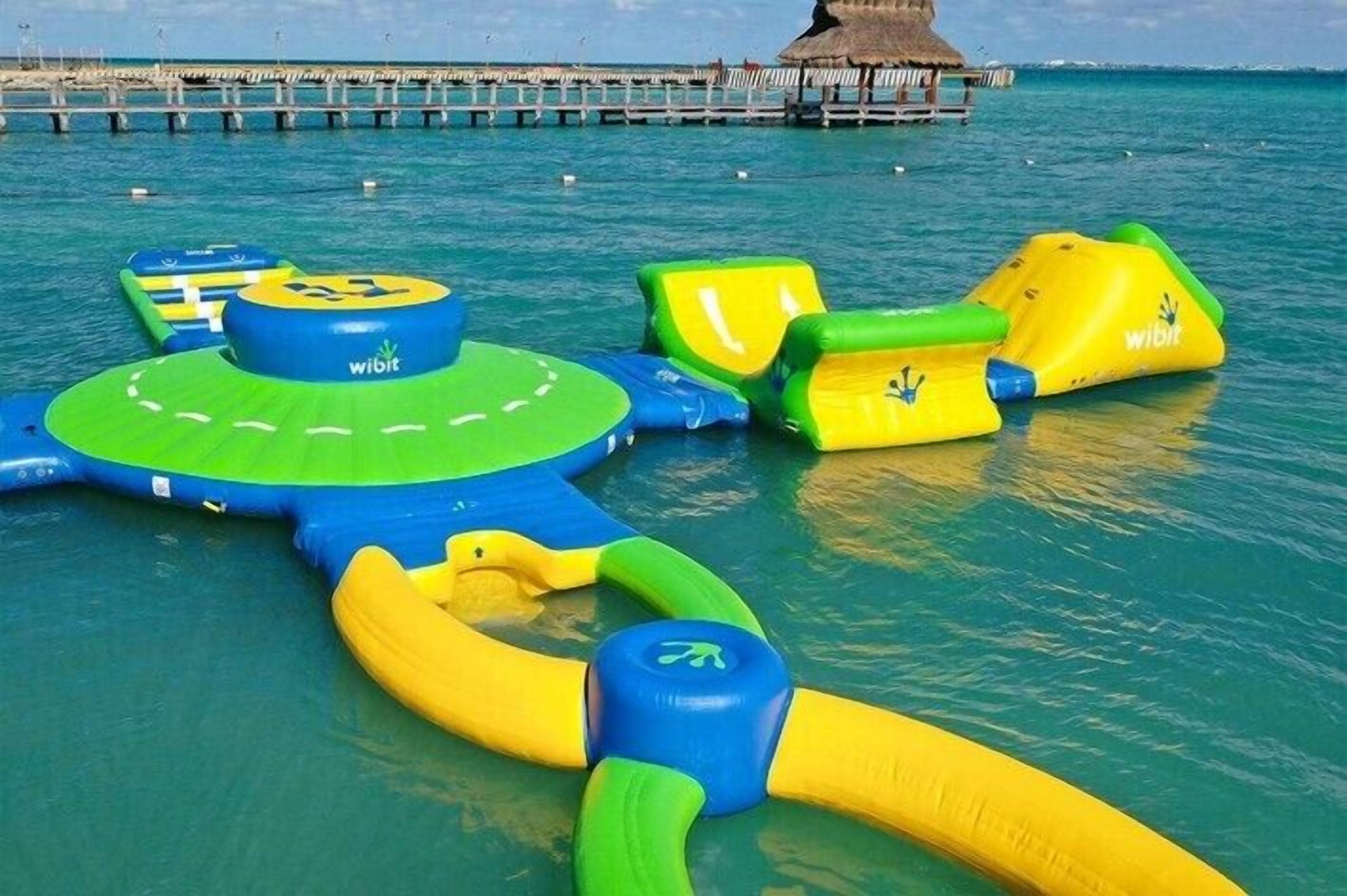 An inflatable water play area with various structures, including a circular platform and slides, in a clear blue water setting.