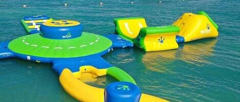 An inflatable water play area with various structures, including a circular platform and slides, in a clear blue water setting.
