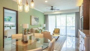 A modern living room with a glass dining table, sofas, a ceiling fan, and a large window with curtains. - Garza Blanca Resort and Spa (Punta Sam)