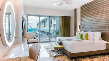 A modern hotel room with a bed, a desk, a chair, a large mirror, and a view of the sea.