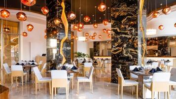 A modern restaurant with round tables, white chairs, and hanging spherical light fixtures.
