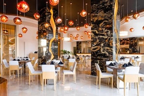 En modern restaurang med runda bord, vita stolar och hängande, sfäriska lampor.