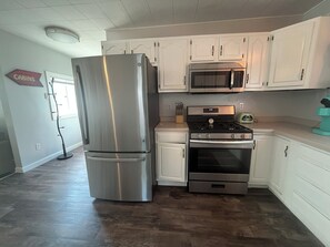 A kitchen with white cabinets, a stainless steel refrigerator, a microwave, and an oven. - Mint Mariner Adorable 2 Bedroom House in Munising (Munising)
