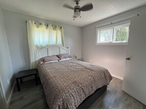 A bedroom with a bed, a bedside table, a window, and a ceiling fan. - Mint Mariner Adorable 2 Bedroom House in Munising (Munising)