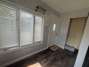 Une pièce avec un plancher en bois foncé, des murs blancs et une porte dotée d’une fenêtre.
