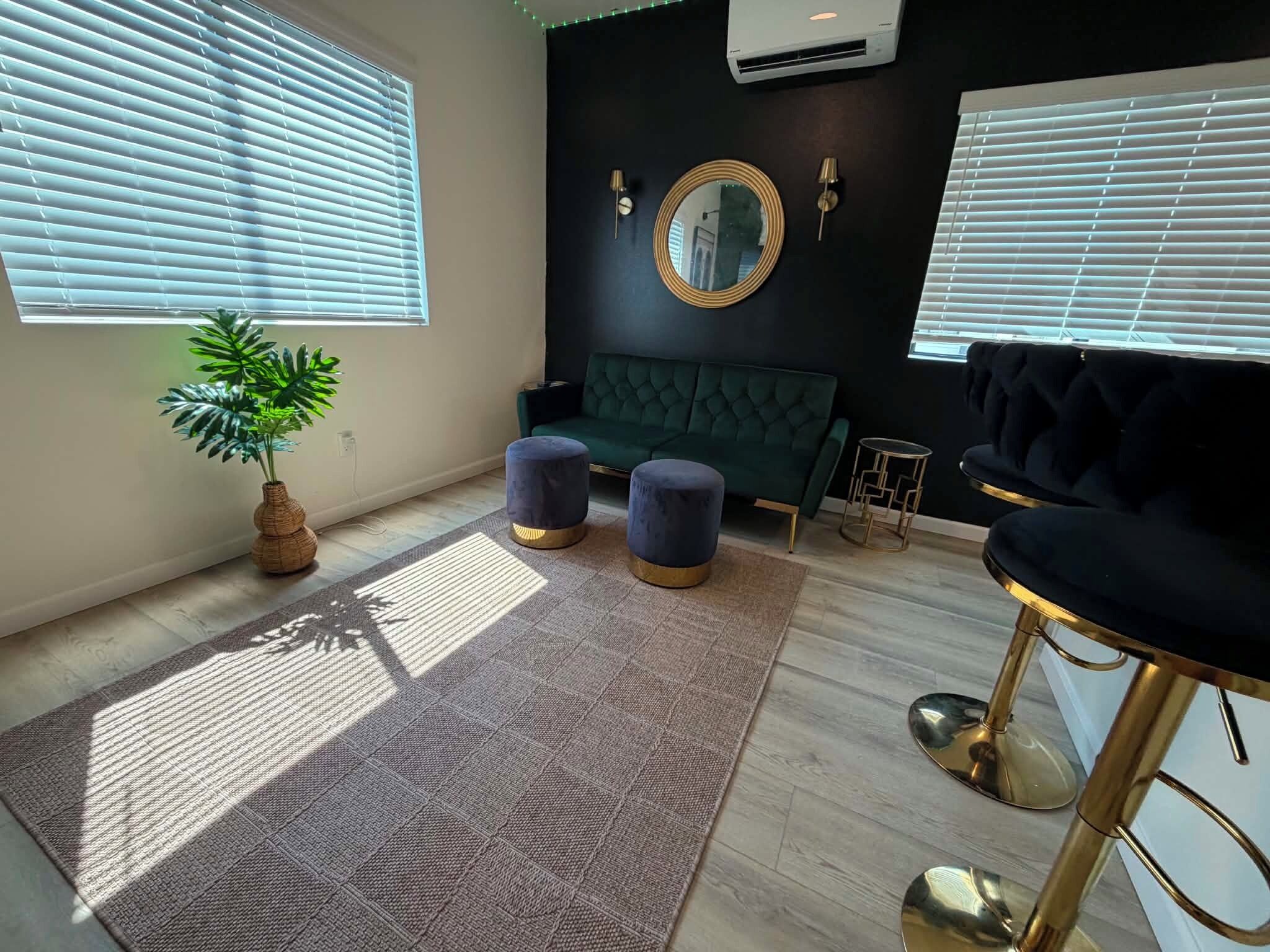 A modern living room with a green sofa, two blue ottomans, a round mirror, and a bar stool.