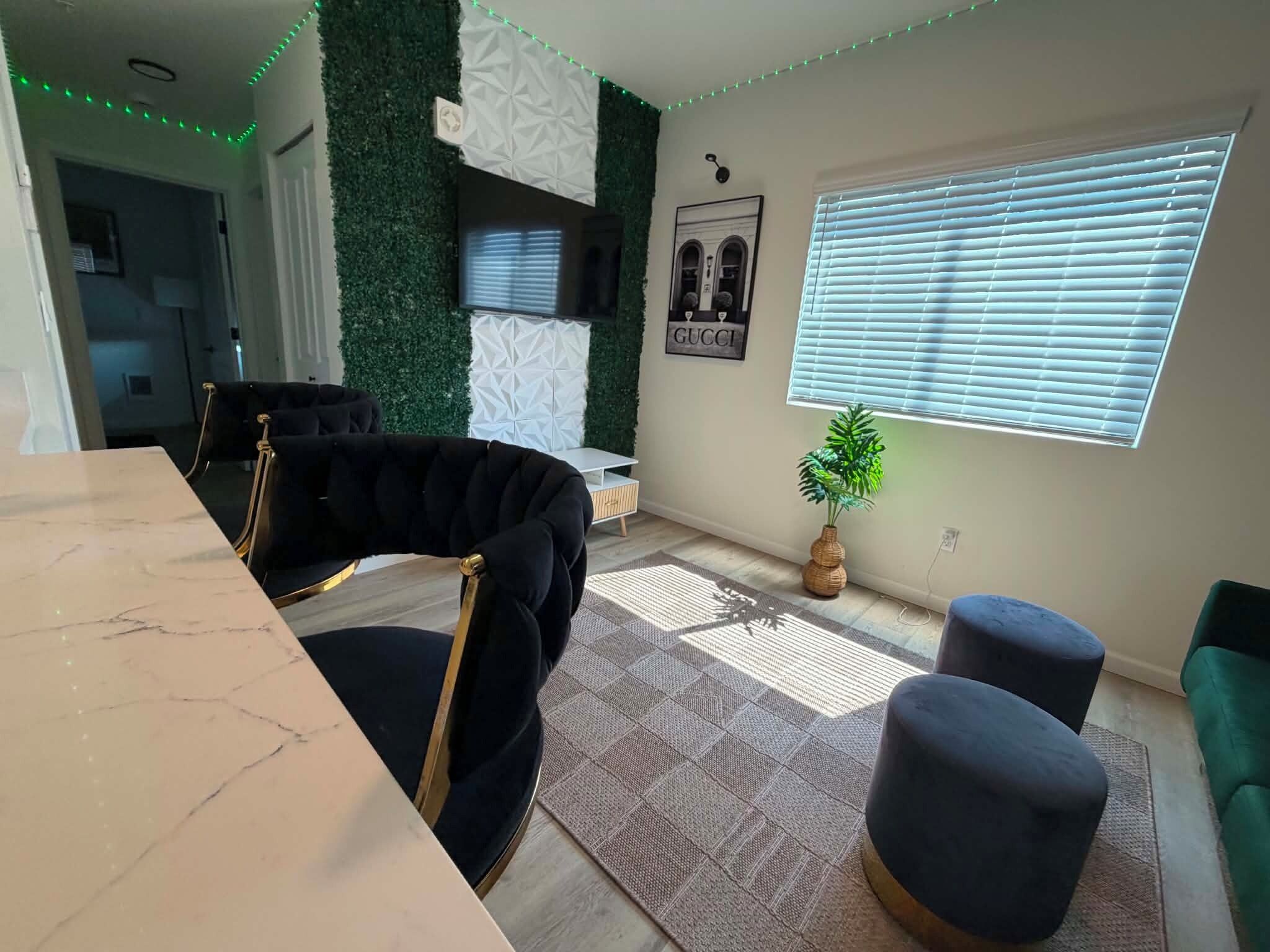 A modern living room with a marble table, black upholstered chairs, a patterned rug, and a green plant.