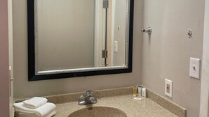A bathroom with a large mirror, a sink, and a towel stack.
