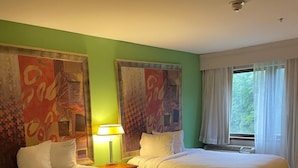A hotel room with two beds, a nightstand with a lamp, and a large window with curtains.