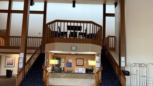 A hotel lobby with a reception desk, two staircases, and a view of the upper floor.