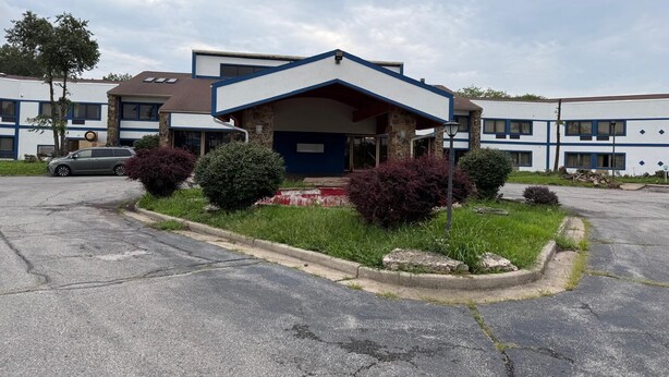 A building with a central entrance, a parking lot, and a car parked in front.