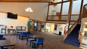 A spacious indoor area with multiple tables and chairs, a staircase, and a chandelier.