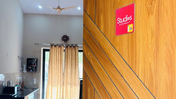 A modern interior with a wooden panel wall, a ceiling fan, and a visible kitchen area with a clock.