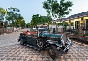 A vintage car parked on a checkered driveway with a house in the background.