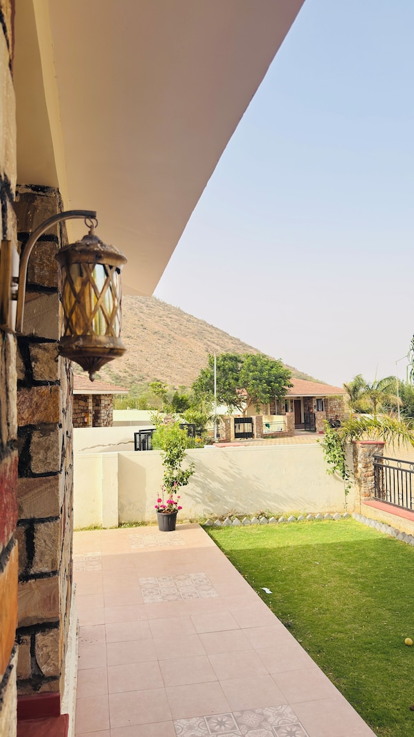 A stone building with a tiled patio, a potted plant, and a view of a hill in the background.