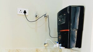 A kitchen with a stainless steel sink, a black refrigerator, and a wall-mounted electrical outlet.