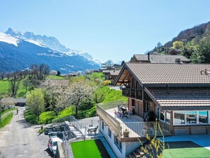 Un chalet moderno con balcón, terraza de madera y vistas a montañas nevadas.