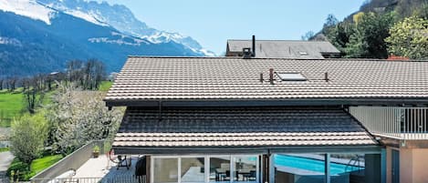Ein modernes Haus mit einer großen Terrasse, einem Schwimmbad und Blick auf die Berge.